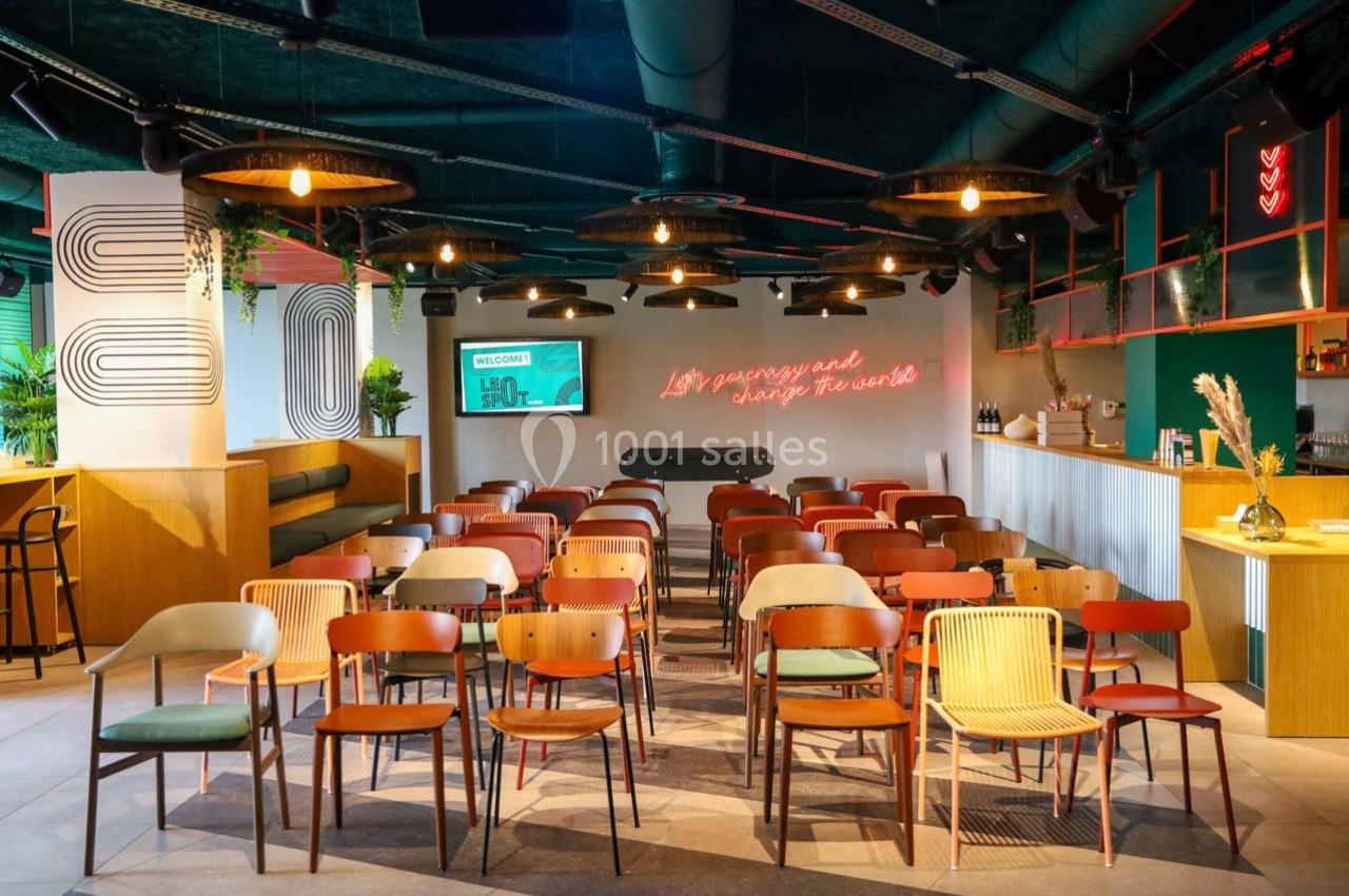 Salle moderne avec des rangées de chaises colorées, un baby-foot au centre et un éclairage chaleureux.