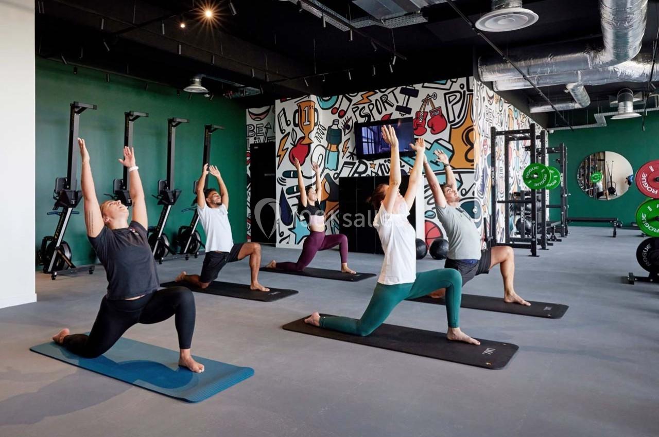 Personnes pratiquant des étirements en salle de sport, sur des tapis, devant un mur décoré de graffitis.