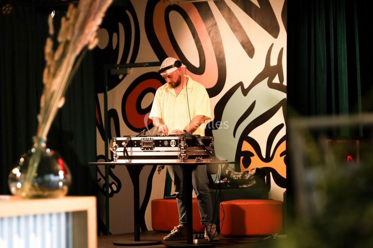 Un DJ mixe sur une table de mixage dans un espace intérieur avec un mur décoré de graffitis en arrière-plan.