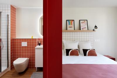 Chambre d'hôtel avec lit double, salle de bain attenante à carreaux rouges et décoration murale colorée.