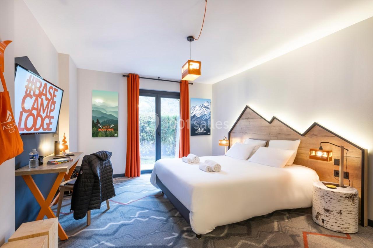 Chambre d'hôtel lumineuse avec lit double, décor montagnard, bureau, et grande fenêtre donnant sur l'extérieur.