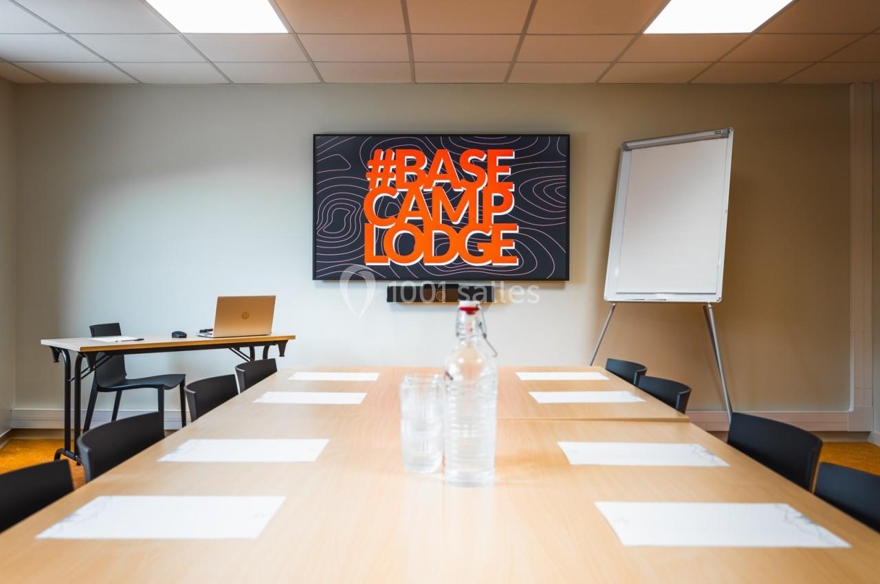 Salle de réunion avec table, chaises, écran affichant ’Base Camp Lodge’, tableau blanc et bouteille d'eau au centre.