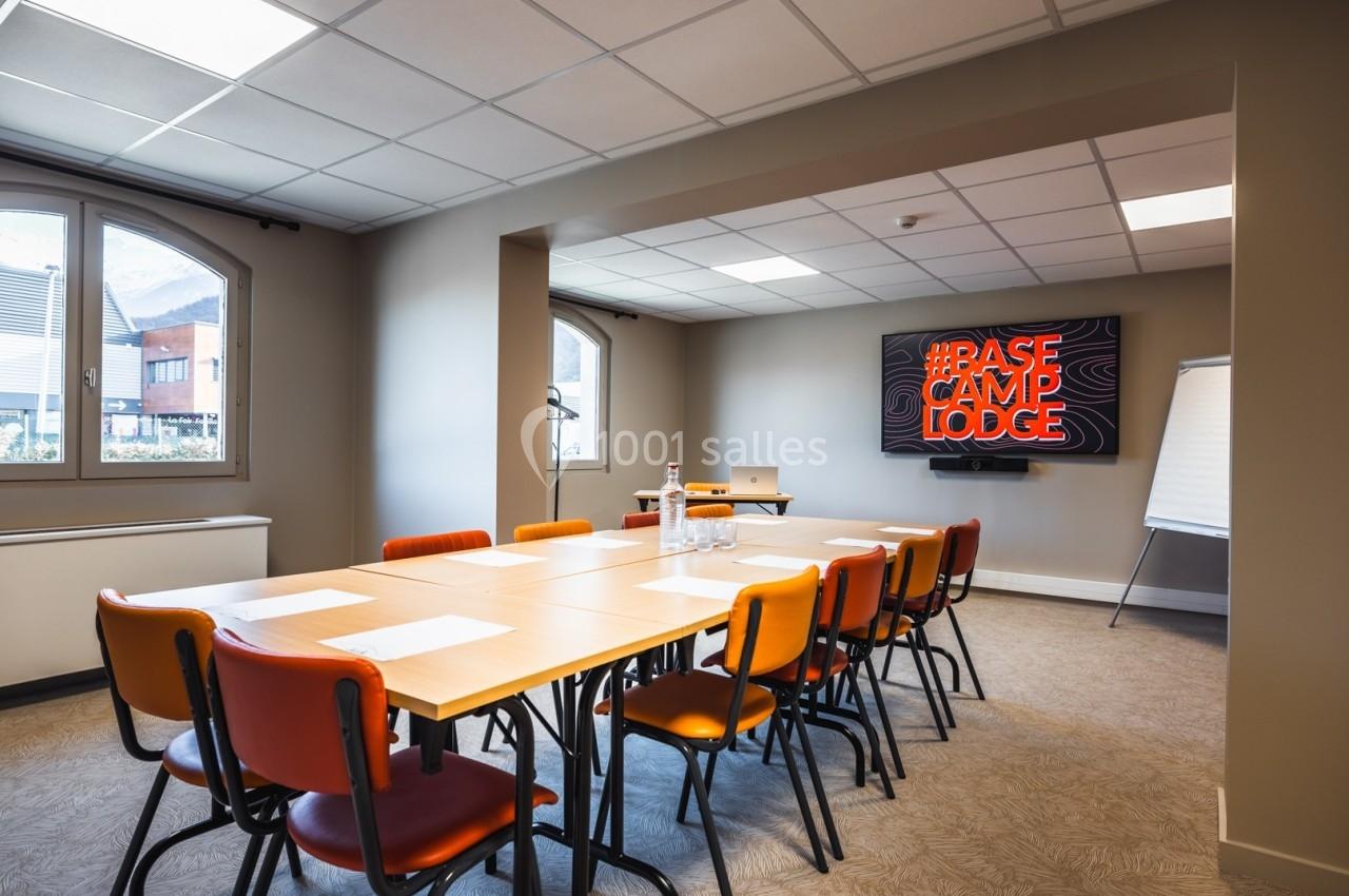 Salle de réunion lumineuse avec table rectangulaire, chaises colorées, écran affichant ’Base Camp Lodge’ et tableau blanc.