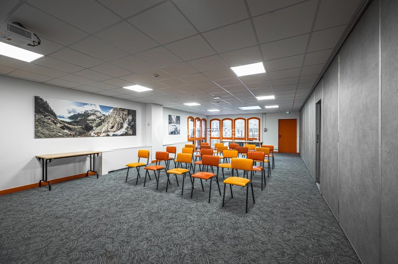Salle de réunion lumineuse avec chaises orange alignées, table en bois et décorations murales représentant des montagnes.