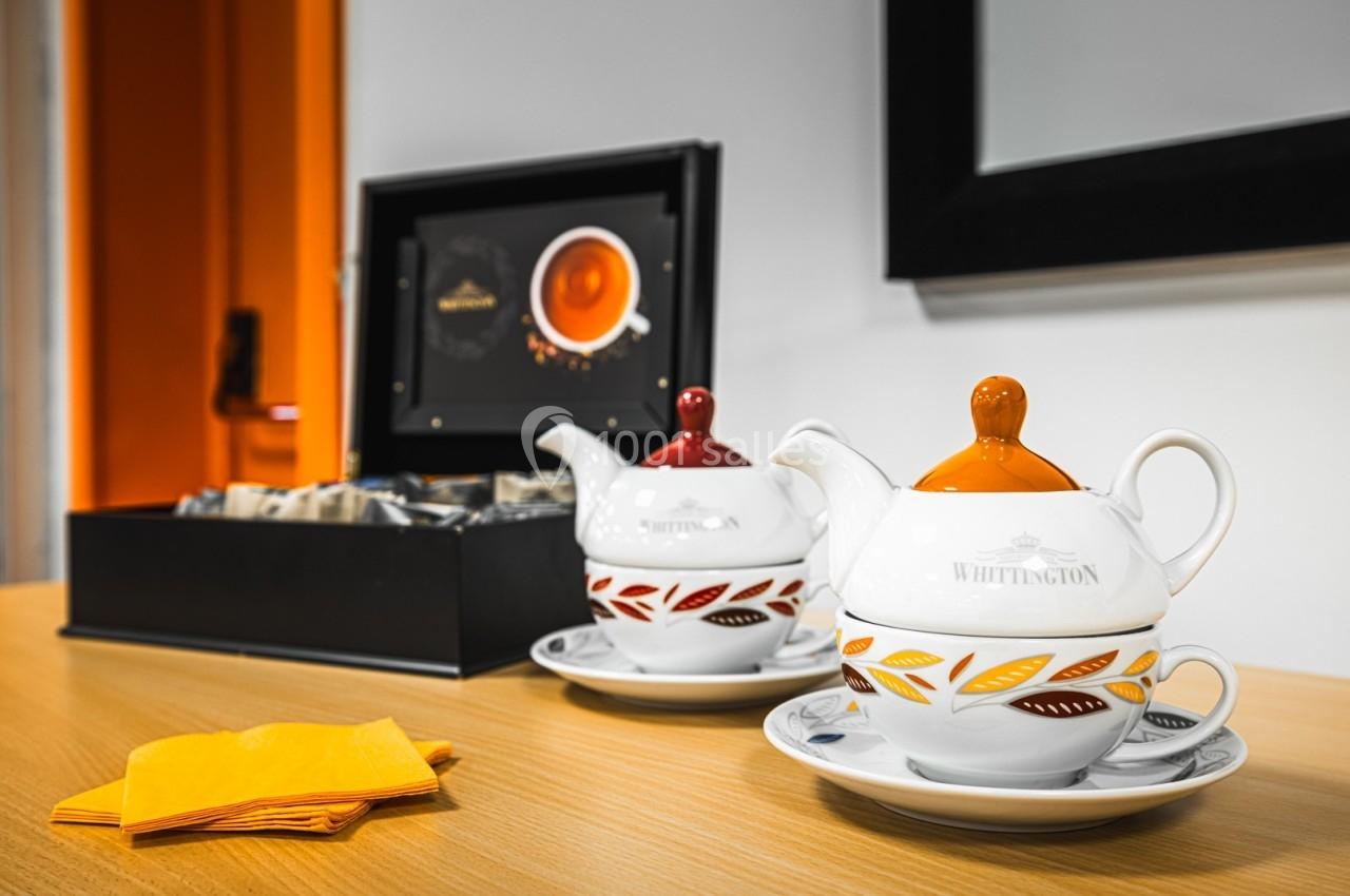 Deux théières blanches décorées de motifs colorés posées sur une table en bois près d'une boîte à thé ouverte.