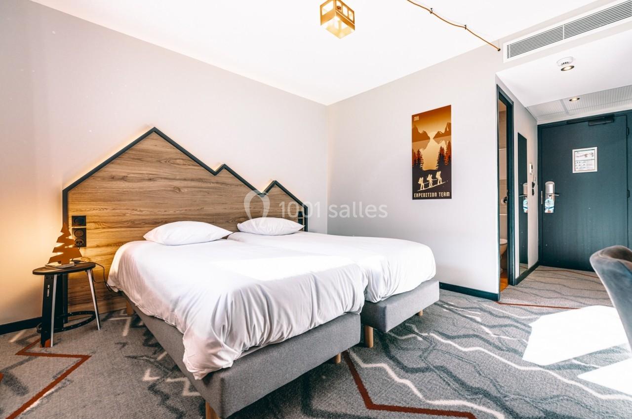 Chambre d'hôtel lumineuse avec deux lits simples, une tête de lit en bois en forme de montagnes et une décoration moderne.