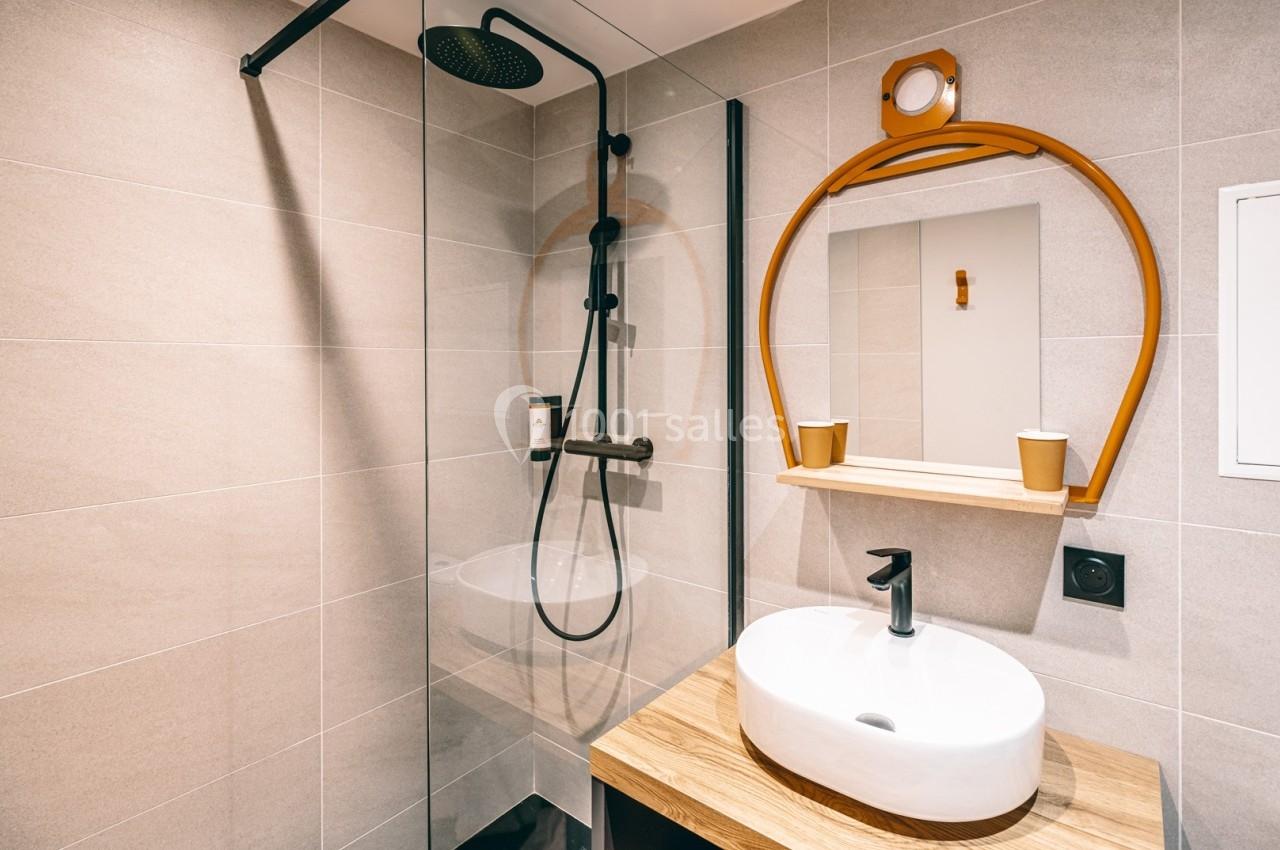 Salle de bain moderne avec douche à l'italienne, lavabo sur meuble en bois et miroir rond encadré d'orange.