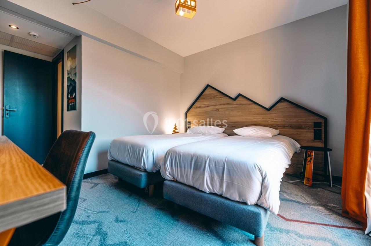 Deux lits simples avec tête de lit en bois, dans une chambre lumineuse avec rideaux orange et décoration moderne.