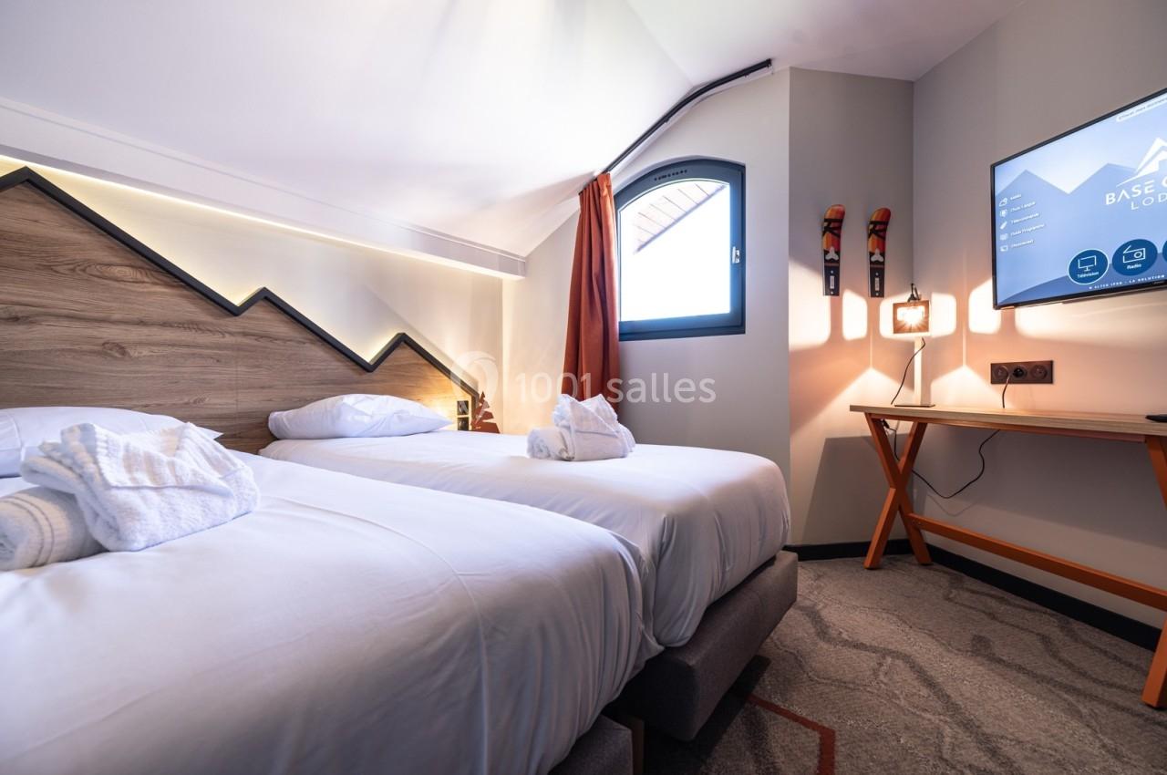 Chambre d'hôtel avec deux lits simples, linge blanc, bureau en bois, télévision murale et fenêtre avec rideau orange.