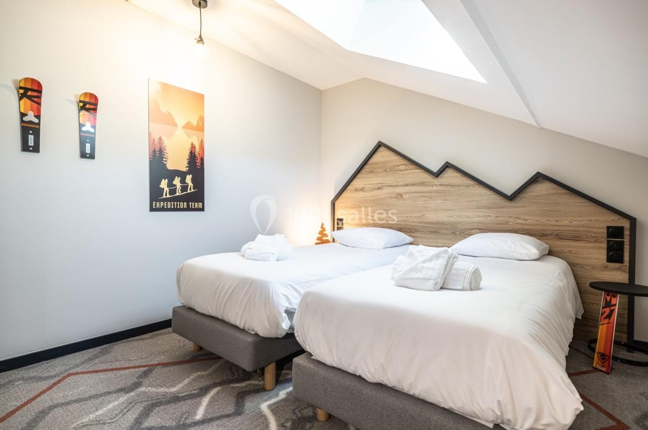 Chambre lumineuse avec deux lits simples, tête de lit en bois en forme de montagne et décoration sur le thème du ski.