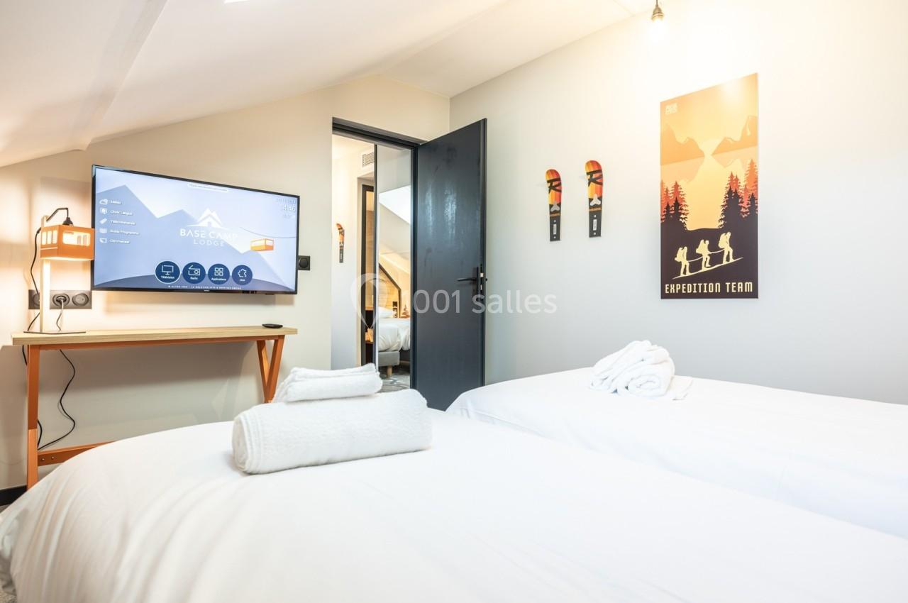 Deux lits avec serviettes pliées, télévision allumée, bureau et décorations murales sur le thème de la montagne.