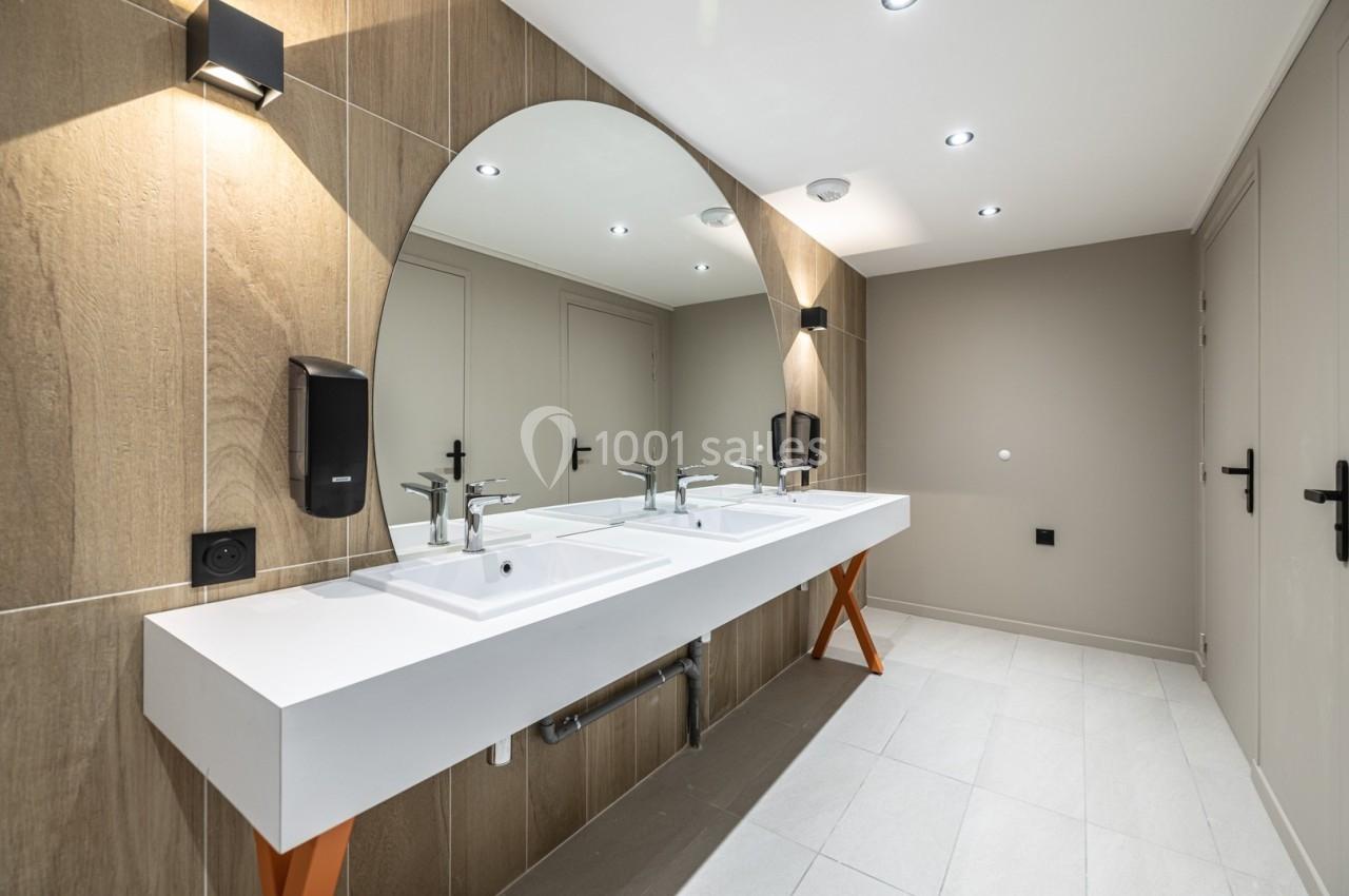 Lavabo double moderne avec miroir arrondi, éclairage encastré et murs en bois clair dans une salle de bain.