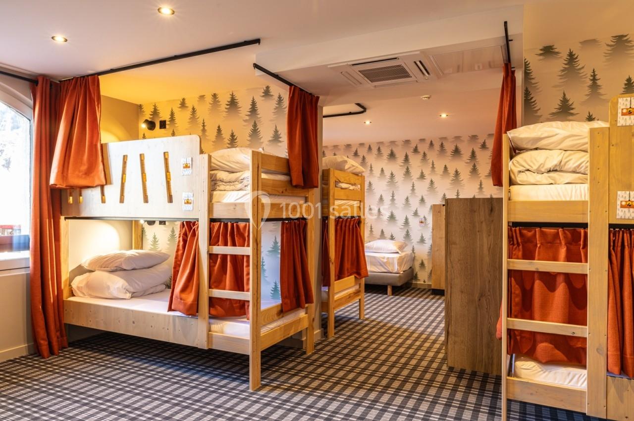 Dortoir avec lits superposés en bois, rideaux orange, murs décorés de motifs d'arbres et sol à carreaux.