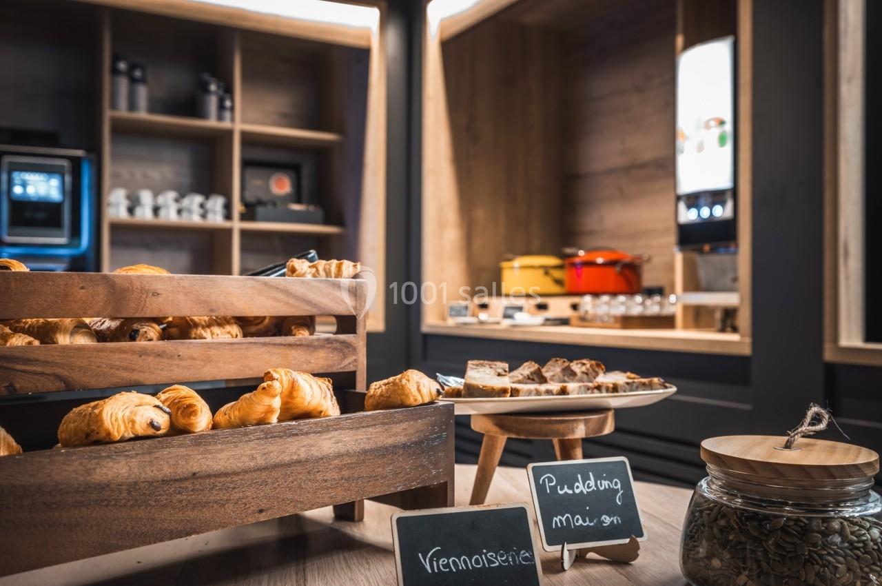 Plateau de viennoiseries en bois, assiette de pudding maison et bocaux dans un espace de buffet lumineux.