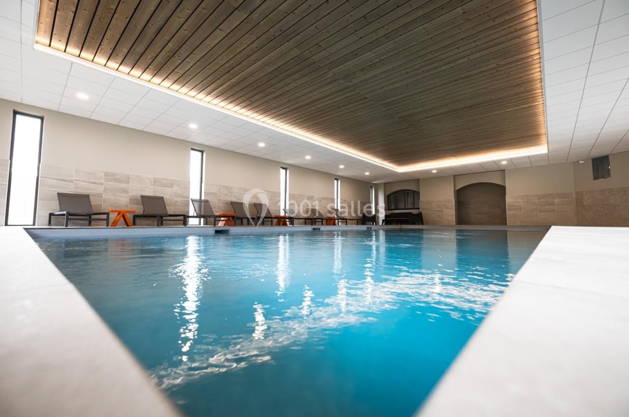 Piscine intérieure avec plafond en bois, chaises longues alignées et éclairage doux.