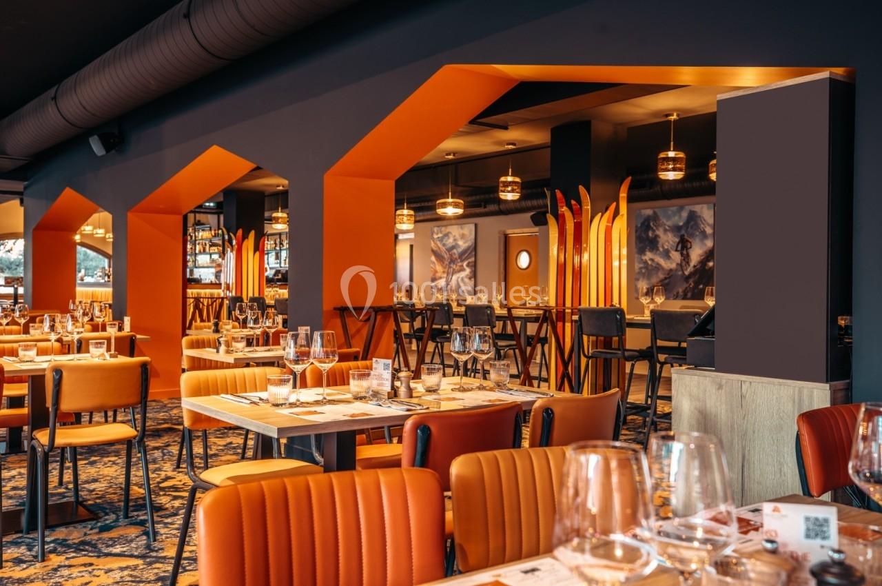 Salle de restaurant moderne avec tables dressées, chaises orange et éclairage chaleureux.