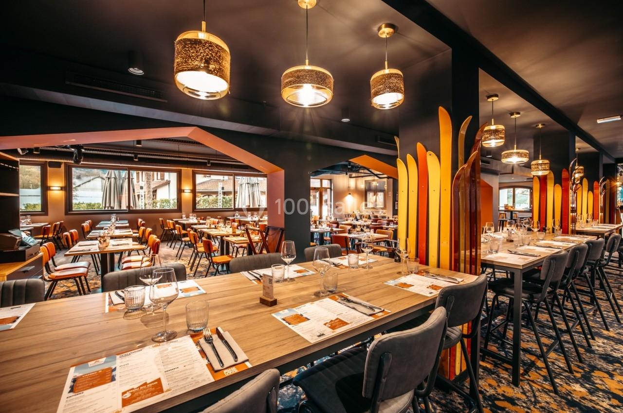 Salle de restaurant moderne avec tables dressées, chaises rembourrées et éclairage chaleureux.