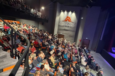 Un groupe de musiciens joue sur scène devant un écran affichant le logo et le slogan ’Base Camp Lodge’.