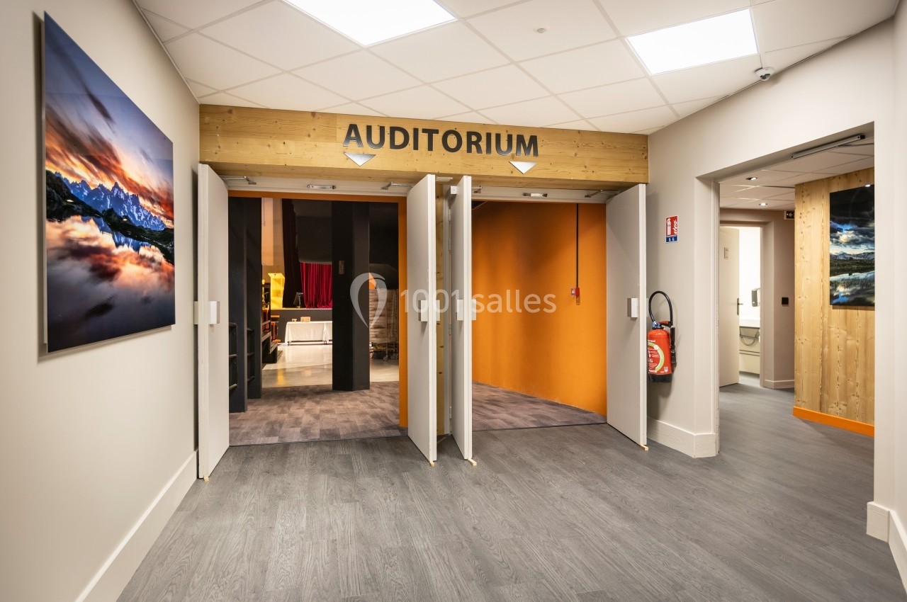 Entrée d'un auditorium avec portes ouvertes, sol en bois, murs clairs et tableaux décoratifs accrochés.