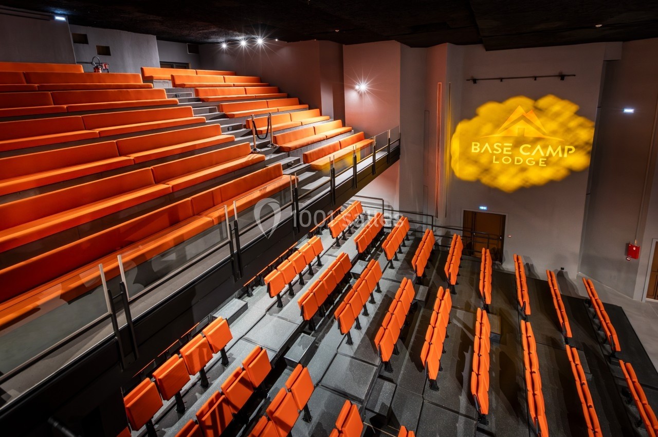 Salle de conférence avec gradins orange, éclairage tamisé et logo projeté sur un mur.