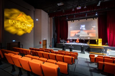 Un groupe de musiciens joue sur scène devant un écran affichant le logo et le slogan ’Base Camp Lodge’.