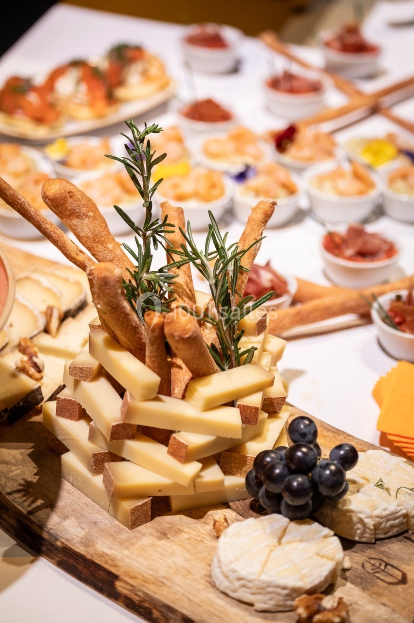 Plateau de fromages variés avec grissini, raisins noirs et noix, entouré de petites assiettes d'accompagnements.