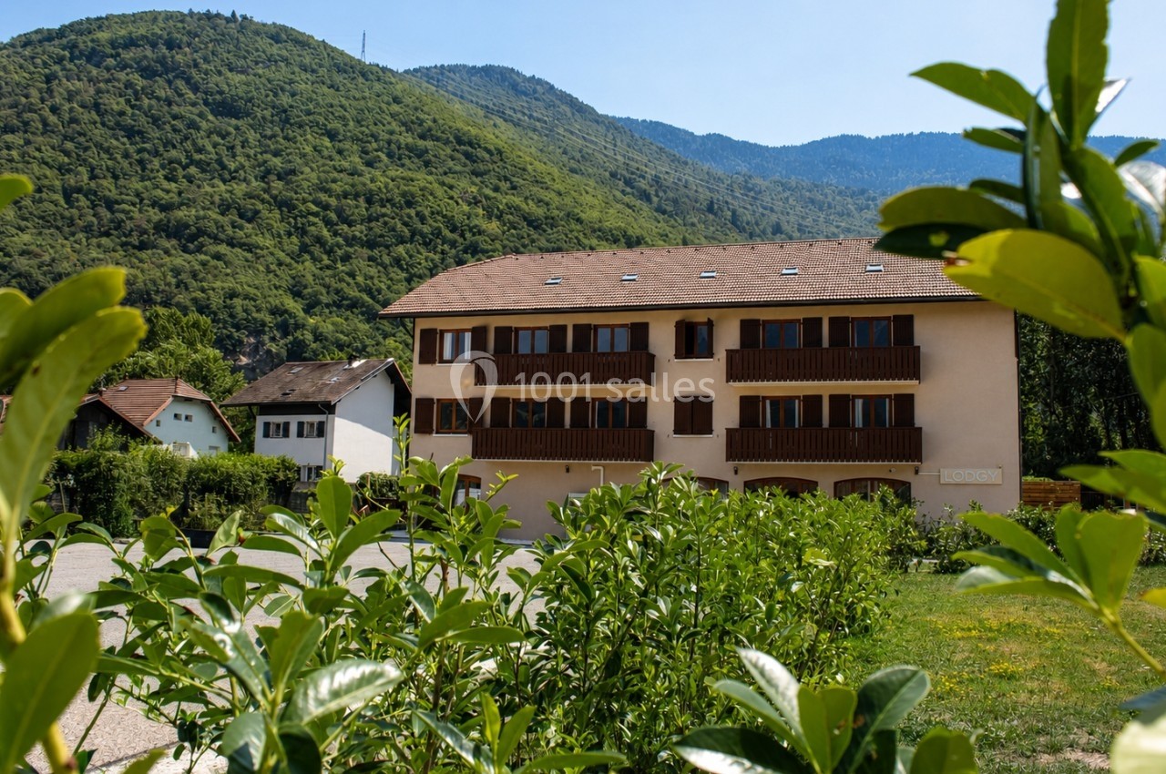 Bâtiment résidentiel beige à trois étages entouré de verdure, avec des collines boisées en arrière-plan.