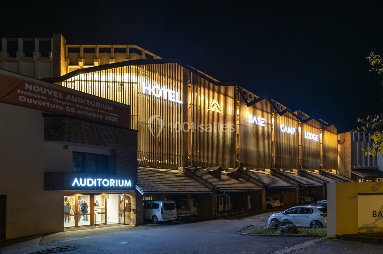 Façade éclairée de nuit d'un hôtel avec enseignes lumineuses ’Base Camp Lodge’ et entrée d'un auditorium.