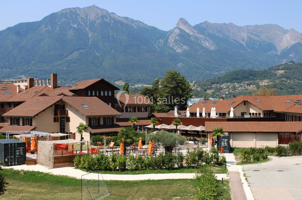 Vue d’un complexe hôtelier avec terrasses et parasols, entouré de montagnes verdoyantes sous un ciel dégagé.