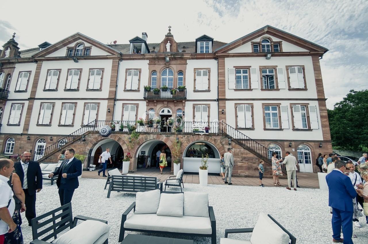 Façade d'un bâtiment historique en pierre avec des escaliers, des fenêtres à volets et une terrasse aménagée.