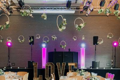 Salle de réception lumineuse avec tables rondes dressées, grandes baies vitrées et structure métallique apparente.