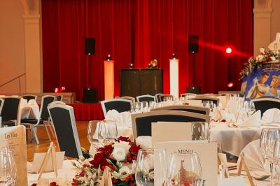 Salle de réception lumineuse avec tables rondes dressées, grandes baies vitrées et structure métallique apparente.