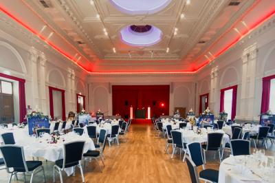 Salle de réception lumineuse avec tables rondes dressées, grandes baies vitrées et structure métallique apparente.