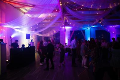 Salle de réception lumineuse avec tables rondes dressées, grandes baies vitrées et structure métallique apparente.