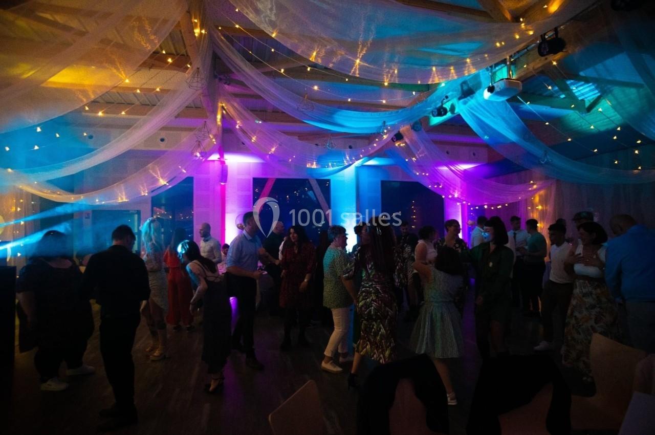 Des personnes dansent sous un plafond décoré de voilages et de lumières colorées dans une ambiance festive.