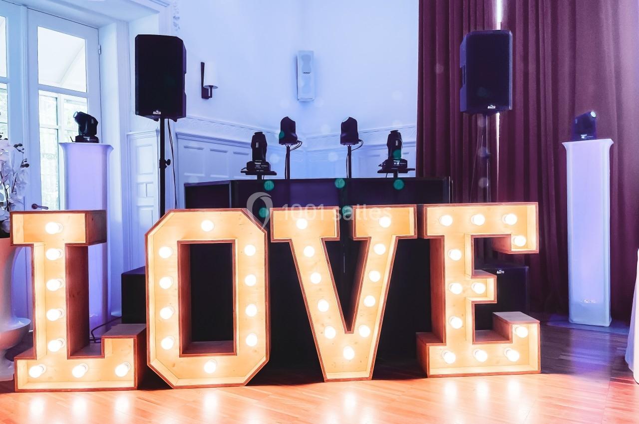Lettres lumineuses formant le mot ’LOVE’ devant une table de DJ dans une salle éclairée par la lumière naturelle.
