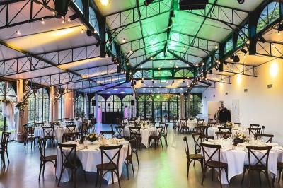 Salle de réception lumineuse avec tables rondes dressées, grandes baies vitrées et structure métallique apparente.