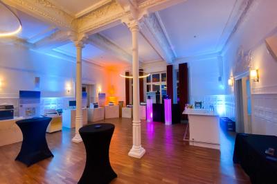 Salle de réception lumineuse avec tables rondes dressées, grandes baies vitrées et structure métallique apparente.