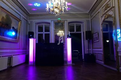 Salle élégante avec parquet, moulures dorées, lustre central et éclairage coloré autour d'une installation DJ.