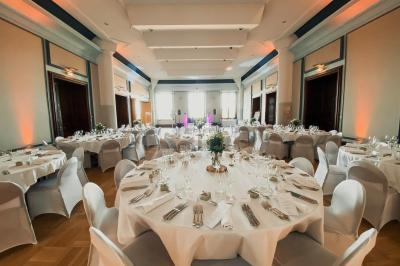 Salle de réception élégante avec des tables rondes dressées, nappes blanches et éclairage chaleureux.