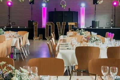 Salle de réception décorée avec des tables dressées, des fleurs suspendues et le mot ’LOVE’ illuminé en arrière-plan.
