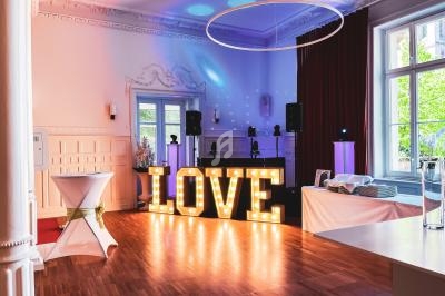 Salle décorée pour un événement avec des lettres lumineuses formant ’LOVE’, une table dressée et un espace DJ.