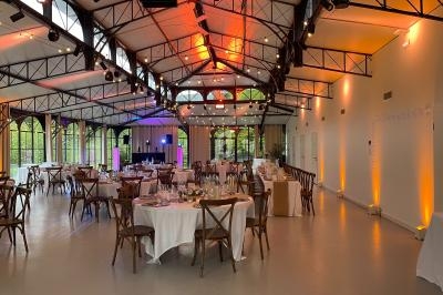 Salle de réception lumineuse avec tables rondes dressées, grandes baies vitrées et éclairage chaleureux.