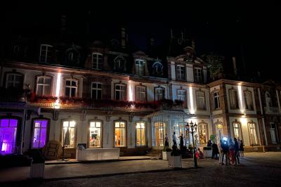 Salle de réception élégante avec tables rondes dressées, décorations florales et lumière naturelle entrant par les fenêtres.