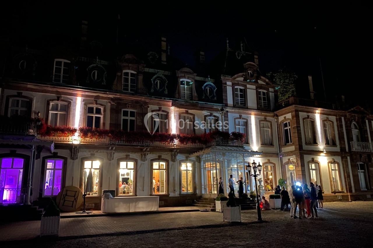 Façade d'un bâtiment éclairé la nuit, avec des lumières colorées et un groupe de personnes rassemblées devant.