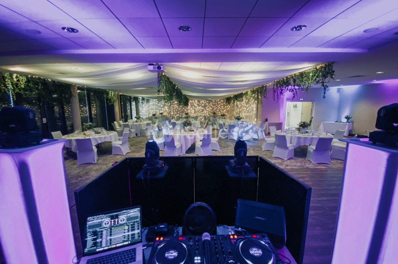 Salle de réception décorée avec des tables dressées, vue depuis une cabine de DJ équipée de matériel audio.