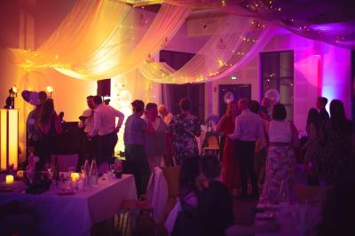 Salle de réception élégante avec tables rondes dressées, décorations florales et lumière naturelle entrant par les fenêtres.