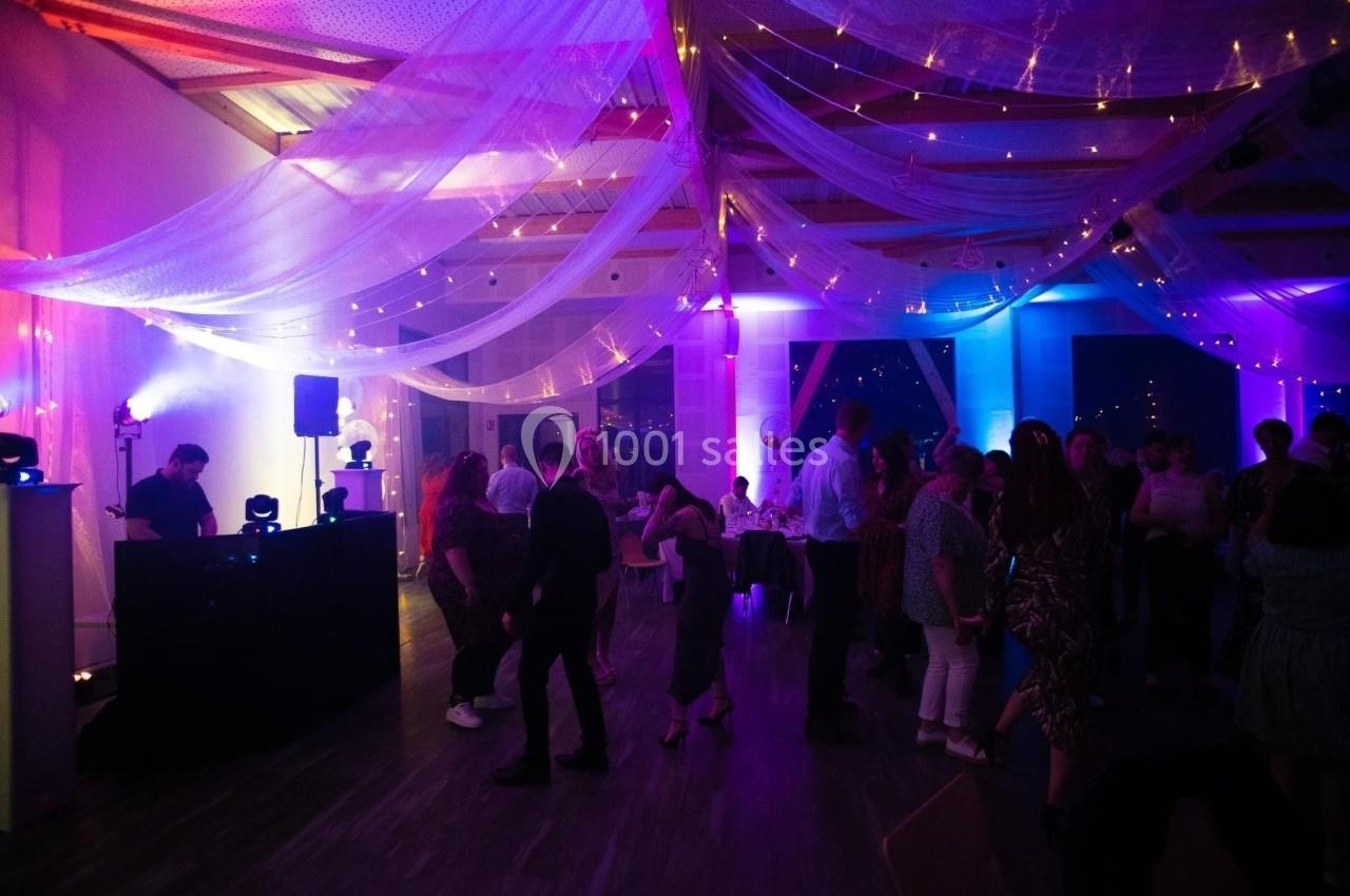 Salle de réception décorée de voilages et lumières colorées, avec des invités dansant et discutant.