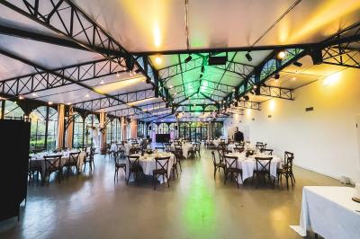 Salle de réception élégante avec tables rondes dressées, décorations florales et lumière naturelle entrant par les fenêtres.