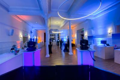 Salle de réception élégante avec tables rondes dressées, décorations florales et lumière naturelle entrant par les fenêtres.
